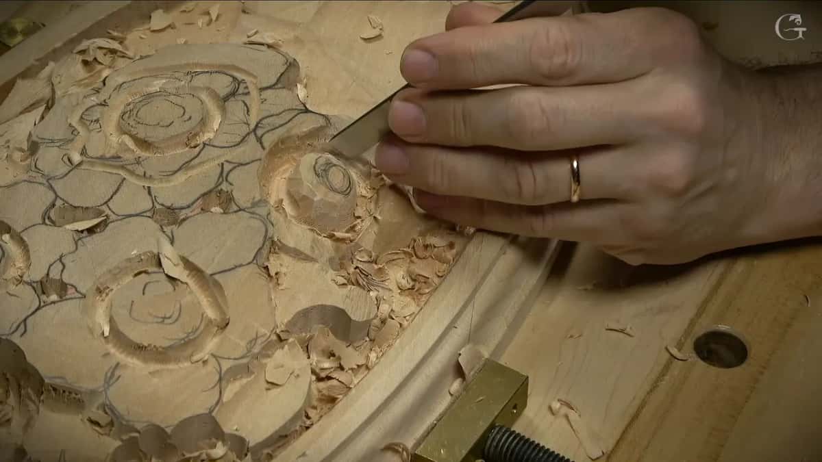 A gouge in his hand trims the ring of one button flower while pencil lines mark the others