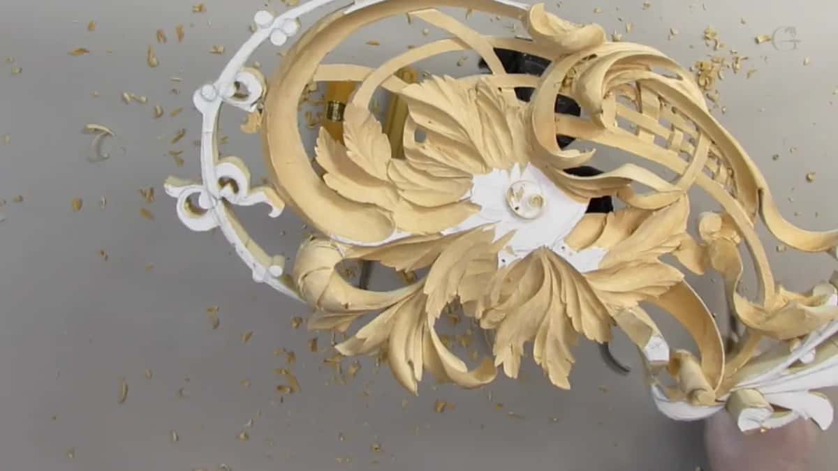 Crossing ribbons over a woven lattice, with a blurred hand at the lower edge of the carving