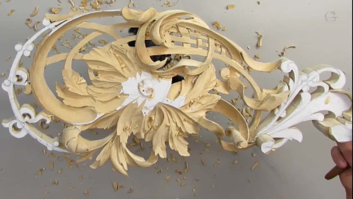 From the other side, the ribbon carving sits on its stand while a hand at the corner holds a tool