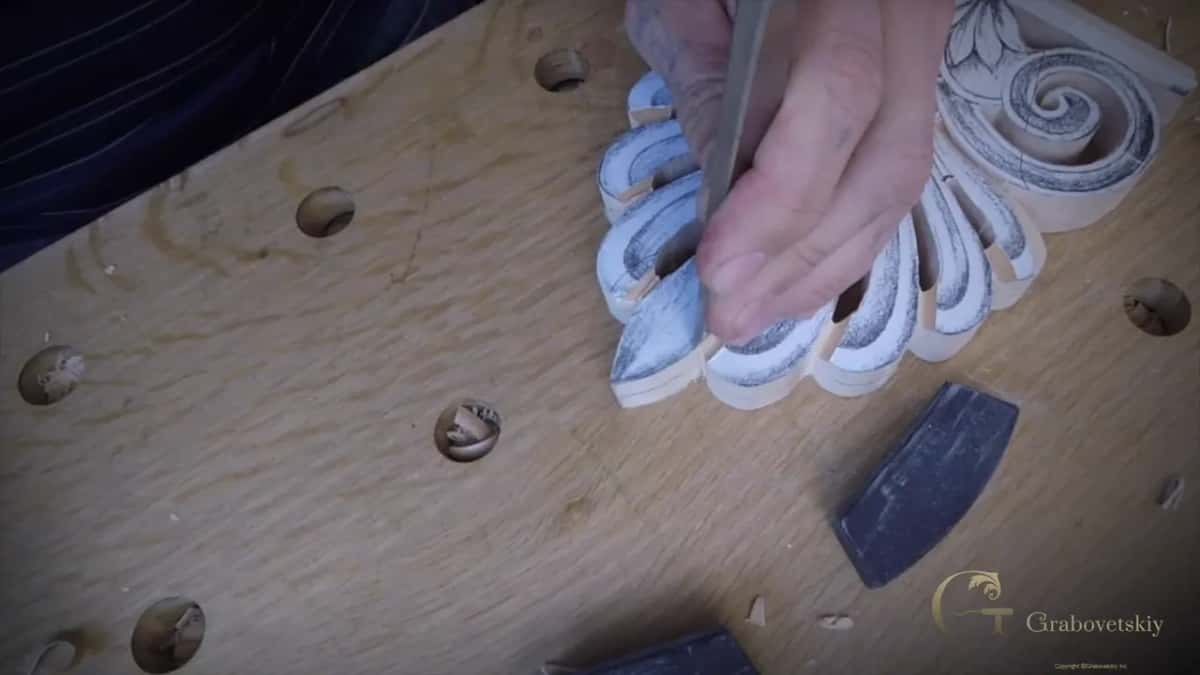 A flat chisel pressed into the line beside a petal, the other hand keeping the fan flat on the bench top
