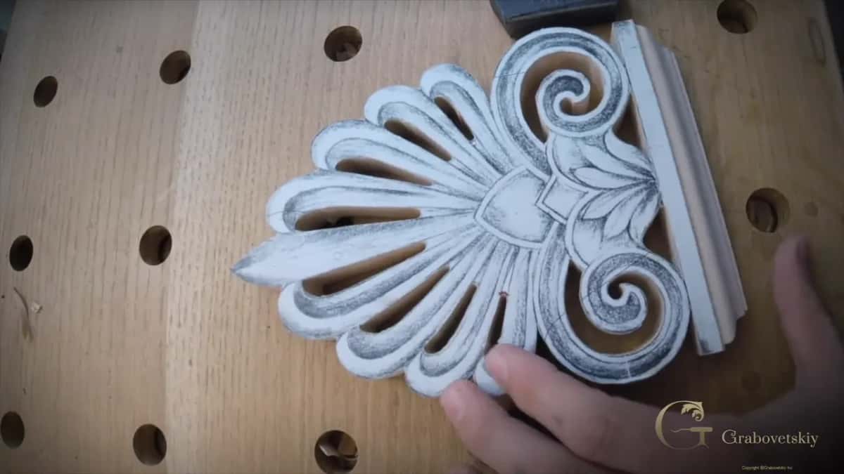 Sawn palm fan blank with its paper pattern glued on, the finished base along one side, on a bench full of round holes