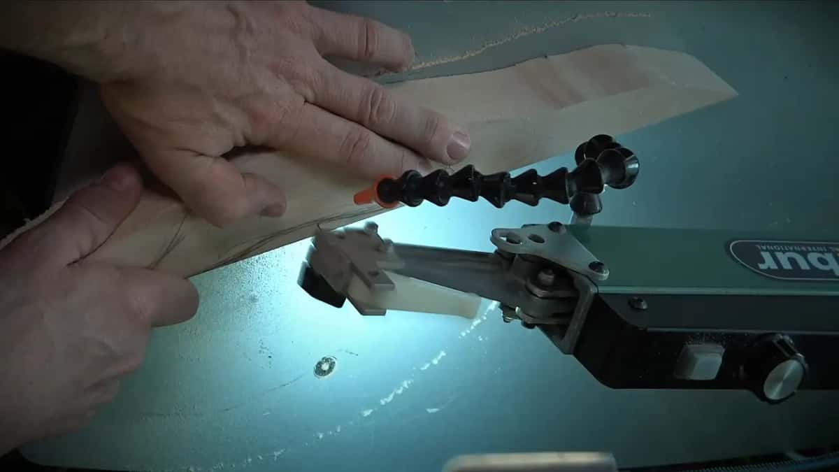 Sawdust trails along a curved drawn line as both hands turn the board on the scroll saw table