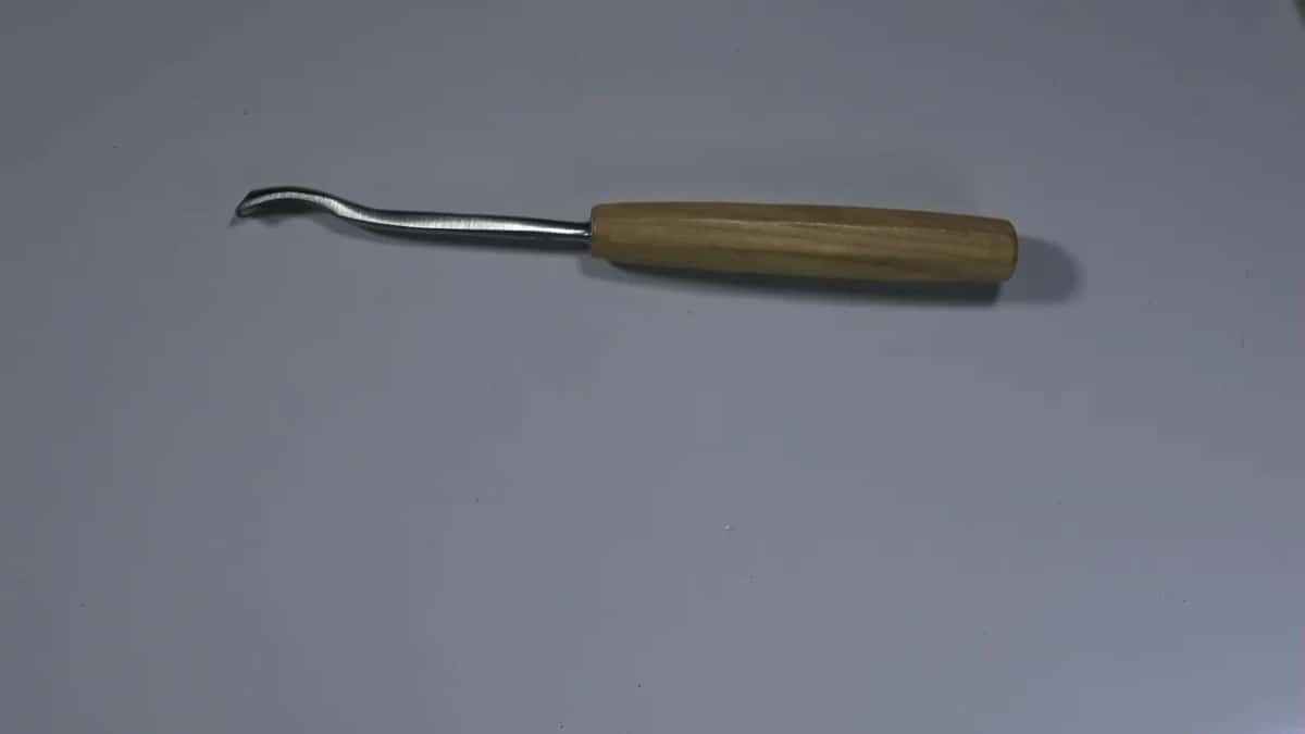 A bent gouge lies on a grey sheet, its pale handle off to the right