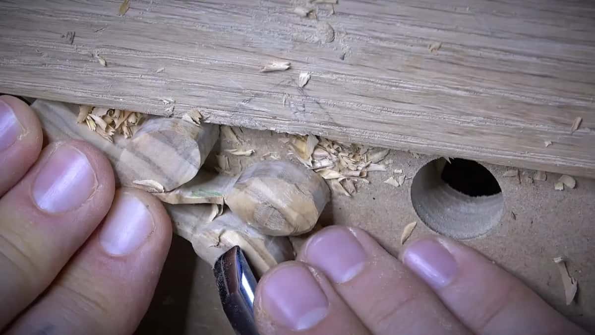 Fingers pinch small carved olives while a gouge works close to them, beside a drilled hole in the board