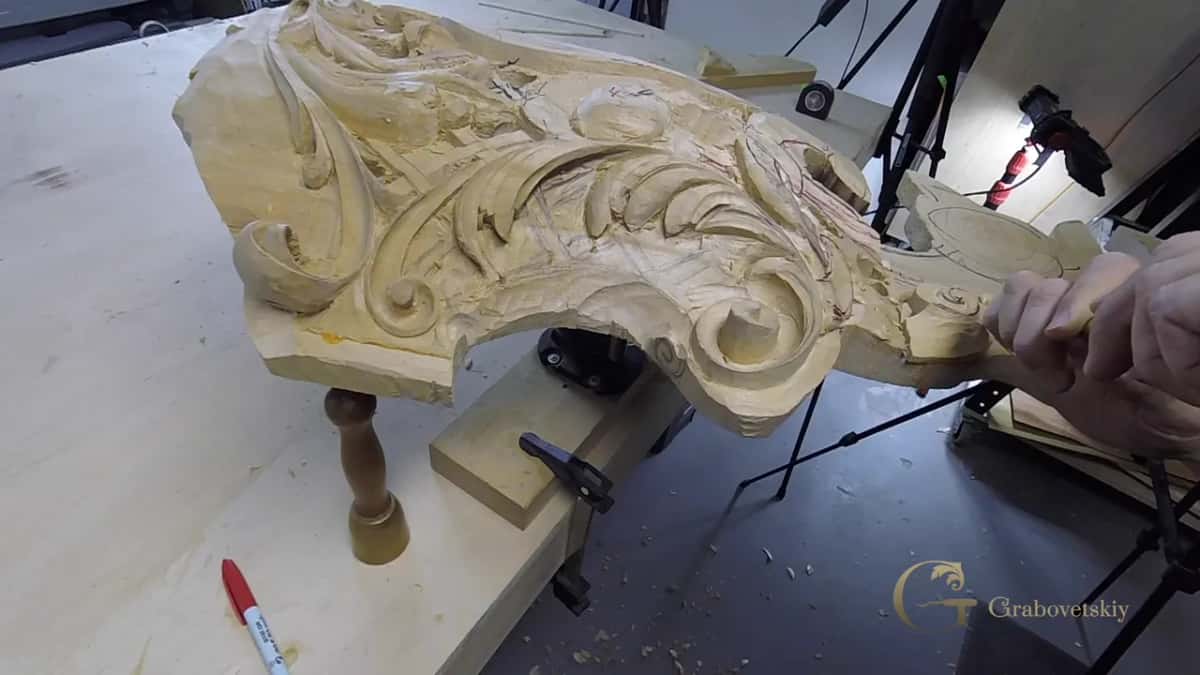 A gouge works along the edge of a large carved scroll