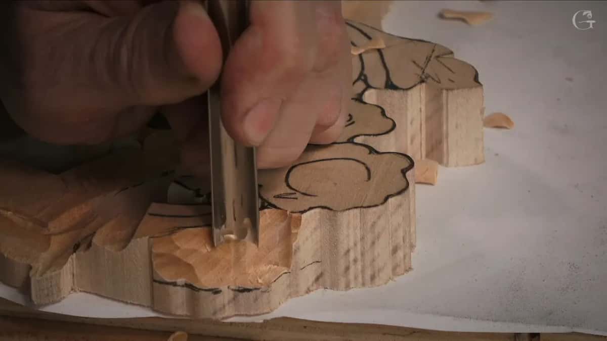 Upright on the black outline of a floral panel blank, a gouge sits with the other hand pressing beside its shank