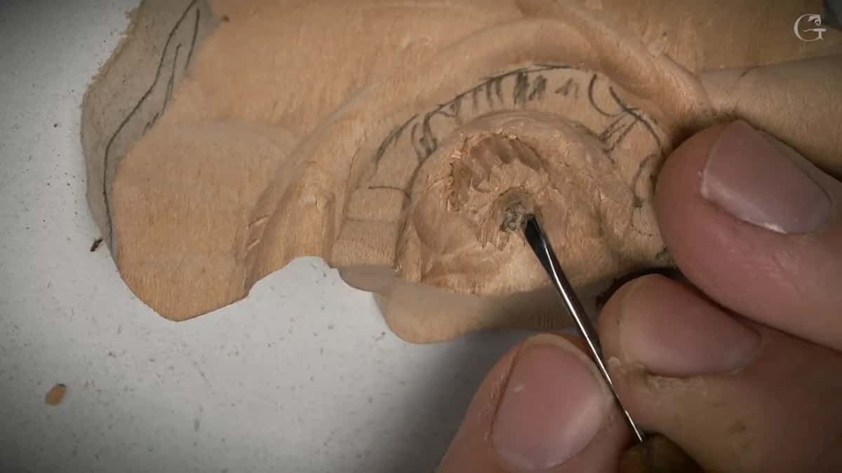 A thin tool works inside the tiny round center of a flower drawn in pencil on a block