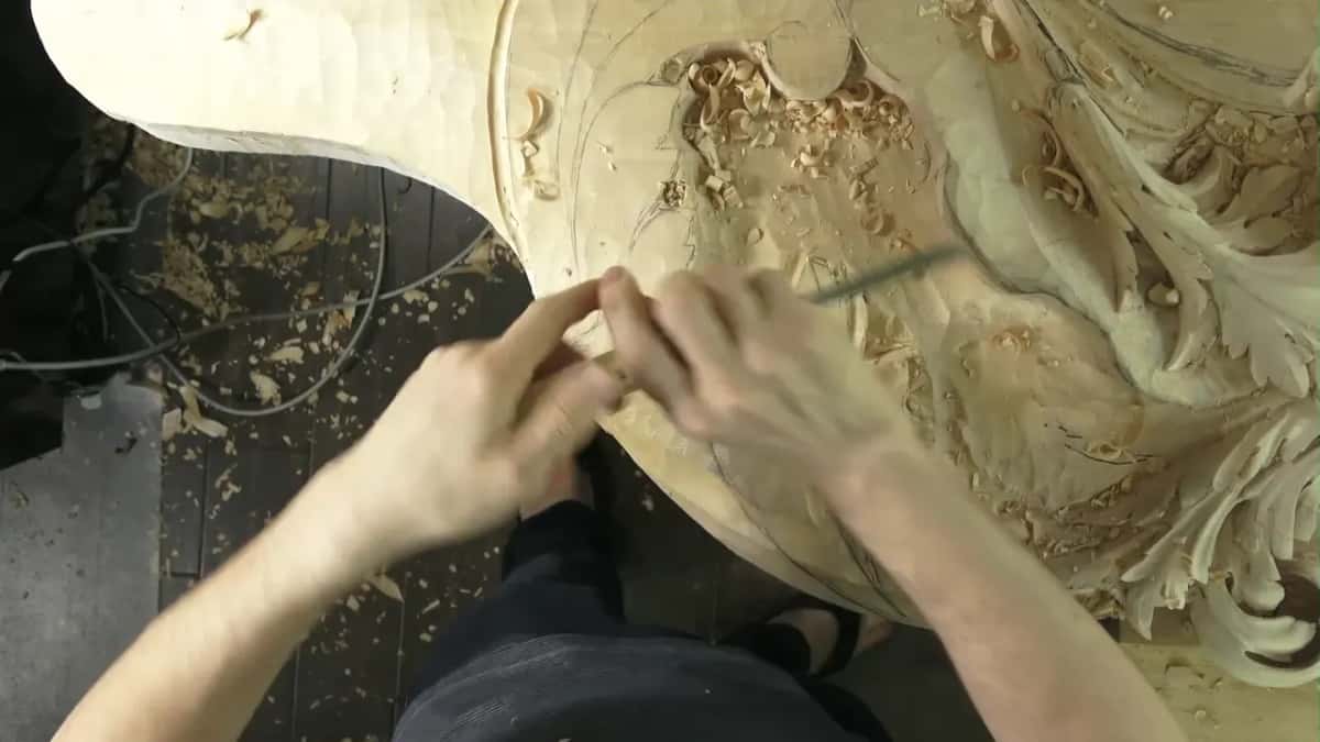 Two hands guide a slim tool across a carved panel