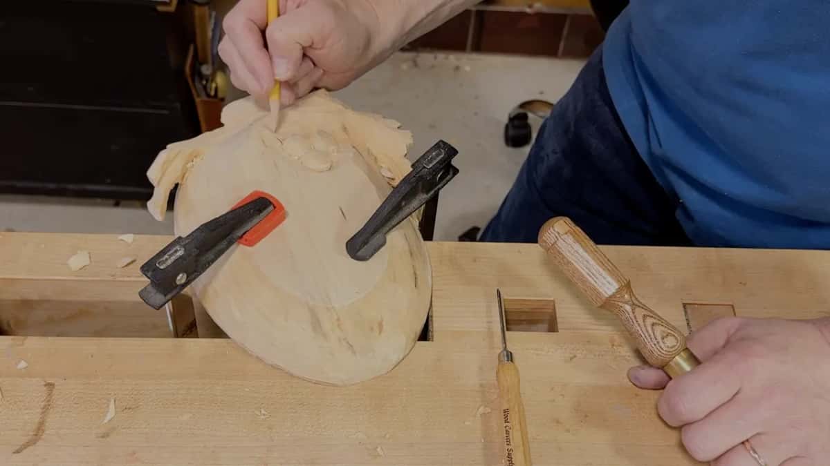 A pencil touches the grapes while the other hand holds a gouge handle against the bench