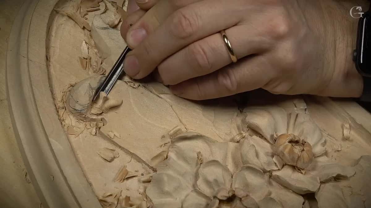 Ring on his finger, he holds a narrow gouge beneath the curled end