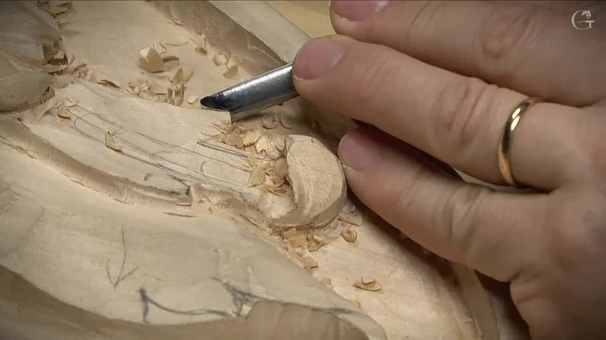 Short curved tool working along a pencil-marked leaf while shavings pile up around a rounded curl