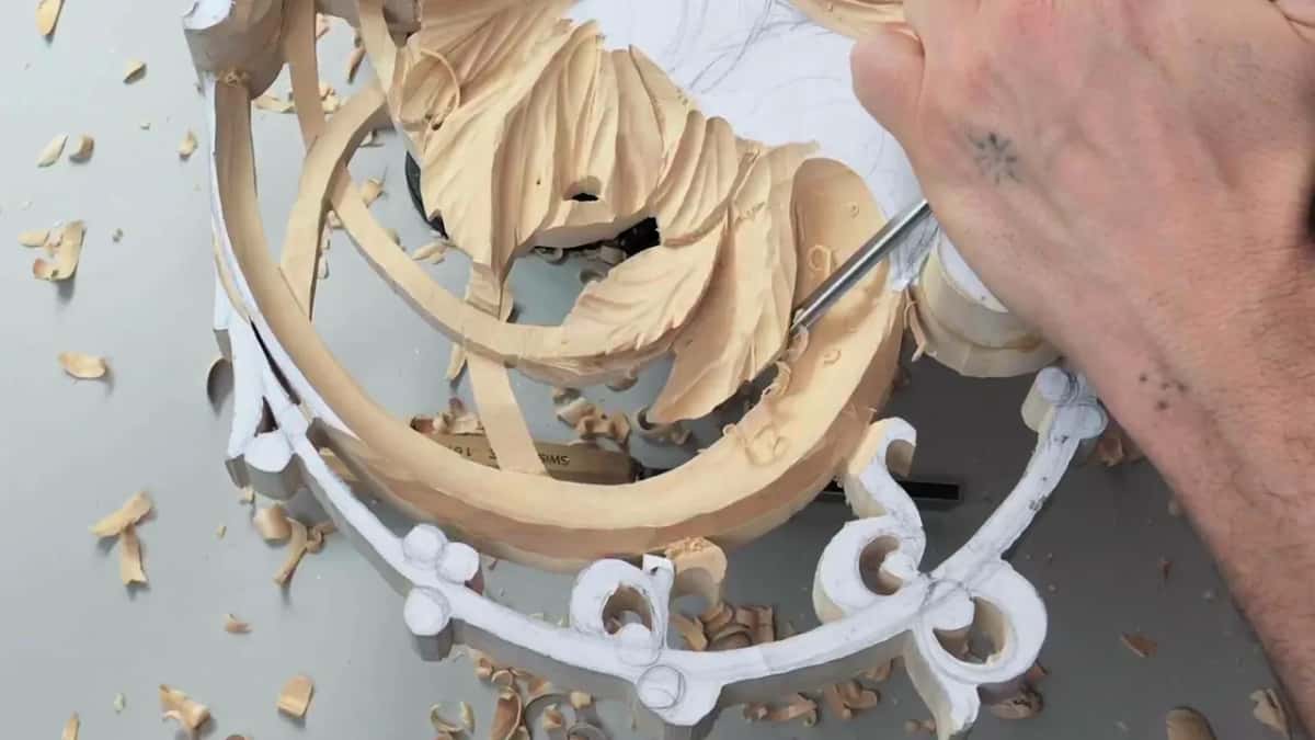 Thin tool working between carved leaves on a pierced panel ringed with white painted scrolls