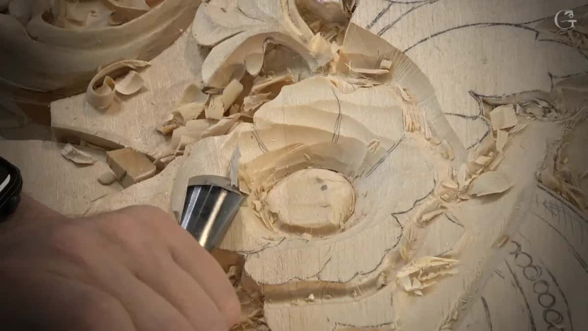 Hand guides a gouge near the round middle, petals marked in pencil