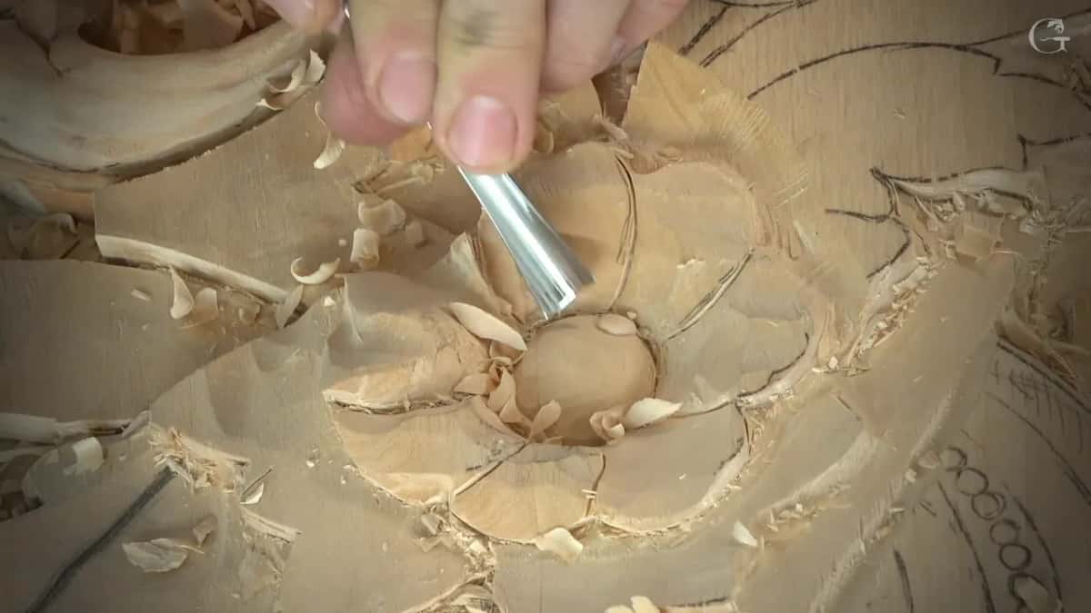 Fingers pinch a gouge blade inside one petal
