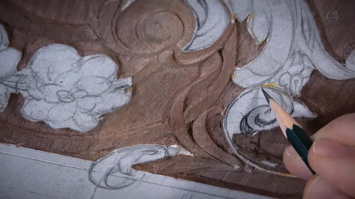 Pencil redraws a scroll on the half carved panel