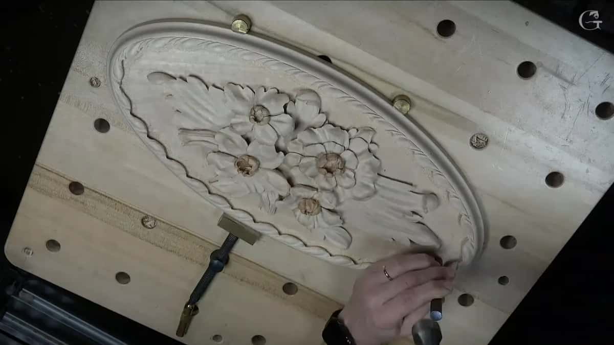 Fingers hold a steel punch on the ground beside the carved border