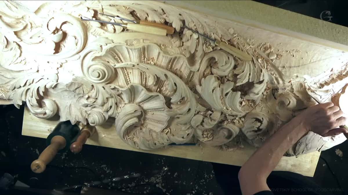 From above, a long carved panel with a shell and acanthus scrolls, gouges resting on top and a mallet below it