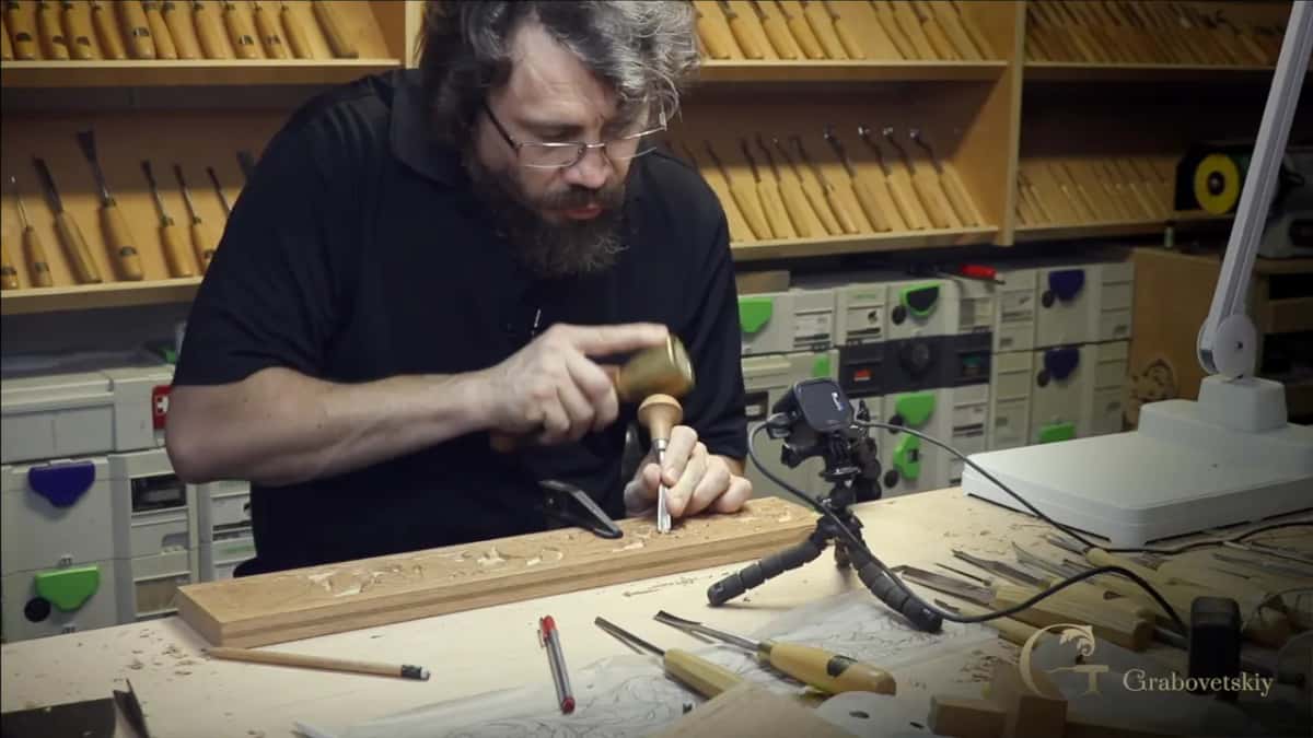 At the bench, a small mallet over a short palm tool, pencils and gouges lying loose by the oak