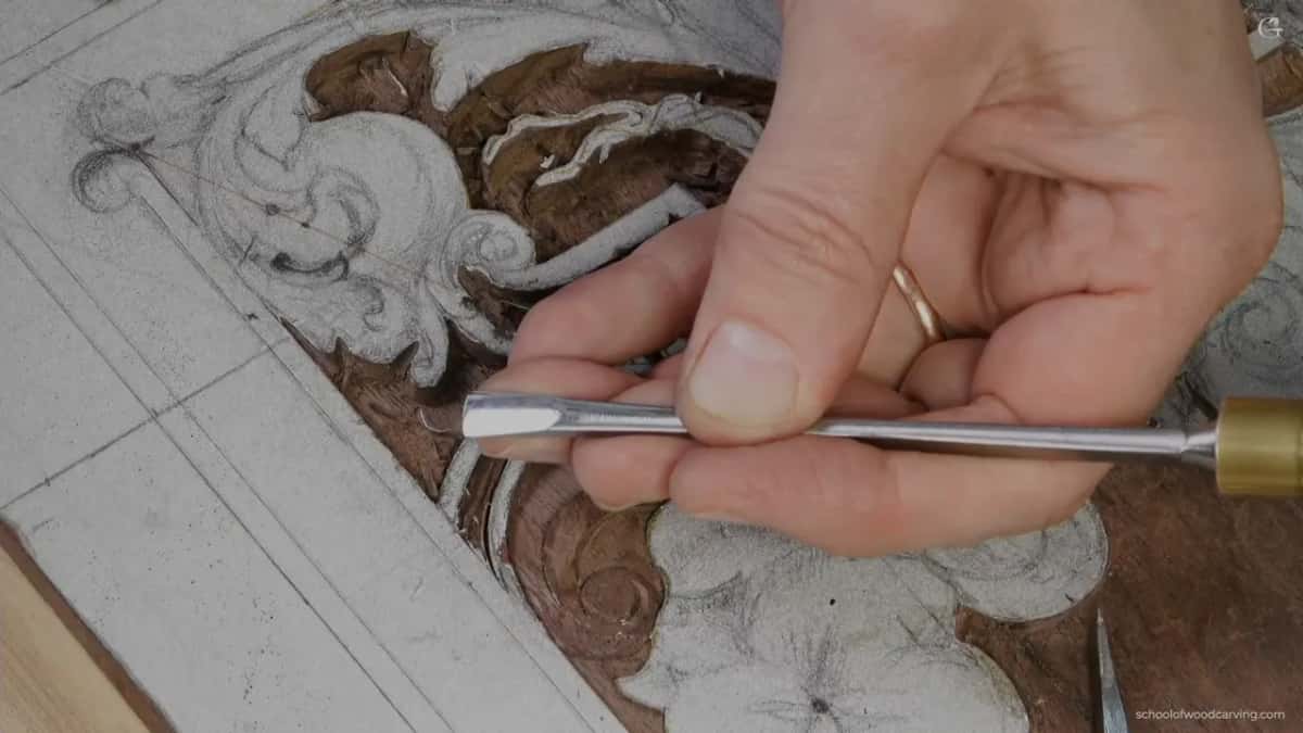 Fingertip close to the steel of a gouge on dark wood