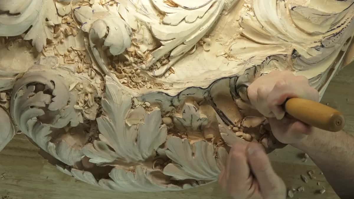 Gouge handle and fingers pressing into the hollow of a big acanthus panel