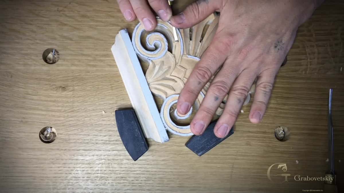 Fingers hold the carved volute still.