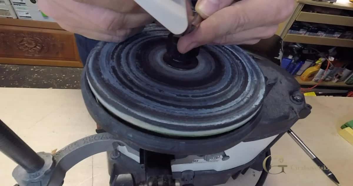 Fingers hold a white stone over a dark wheel while a gouge waits at the side.