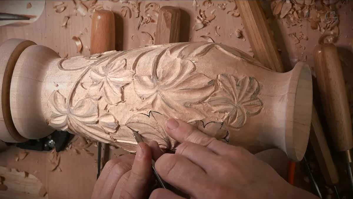 Fingers guide a small blade into a notch while carved leaves wrap the upper body
