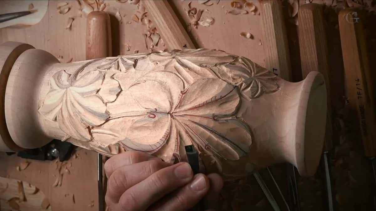 Gouge at a leaf edge, with a rack of carving tool handles standing behind the vase